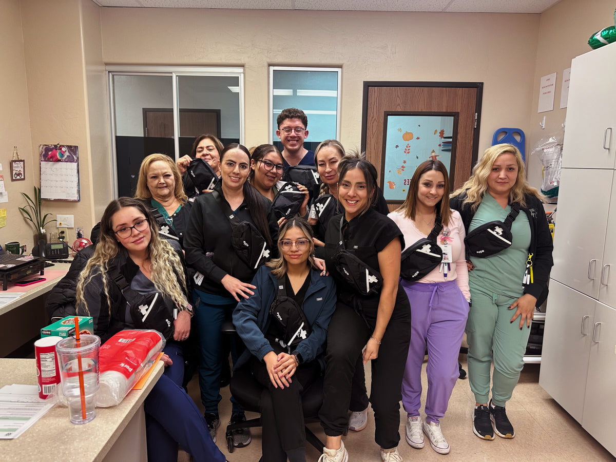 A group of nine healthcare workers wearing matching black and white fanny packs, posing together in a clinical office setting.