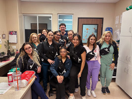 A group of nine healthcare workers wearing matching black and white fanny packs, posing together in a clinical office setting.