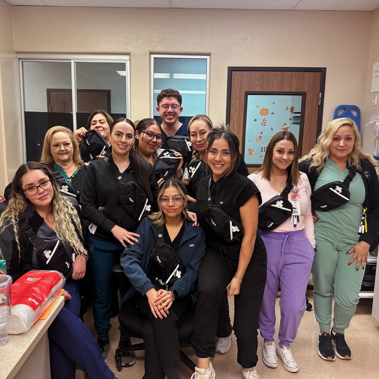 A group of nine healthcare workers wearing matching black and white fanny packs, posing together in a clinical office setting.